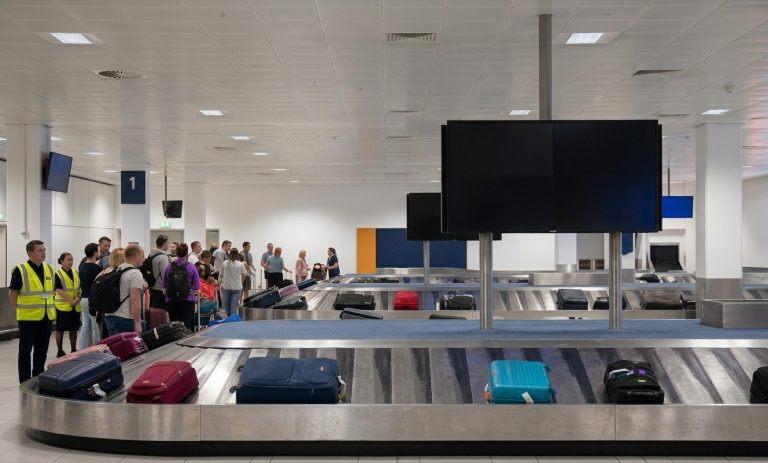 Manchester Airport baggage reclaim area featuring luggage on conveyor belts with terminal signage and passengers waiting in the hall.