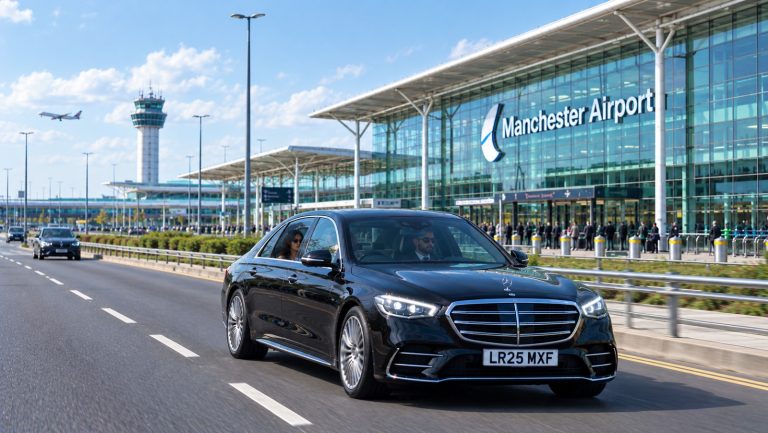 Black Mercedes driving outside Manchester Airport with the terminal, control tower, and airport signage in the background.